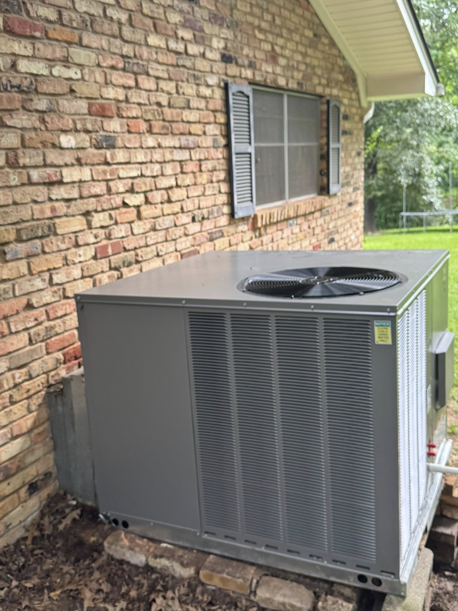 Outdoor HVAC package unit installed against the exterior brick wall of a residential home