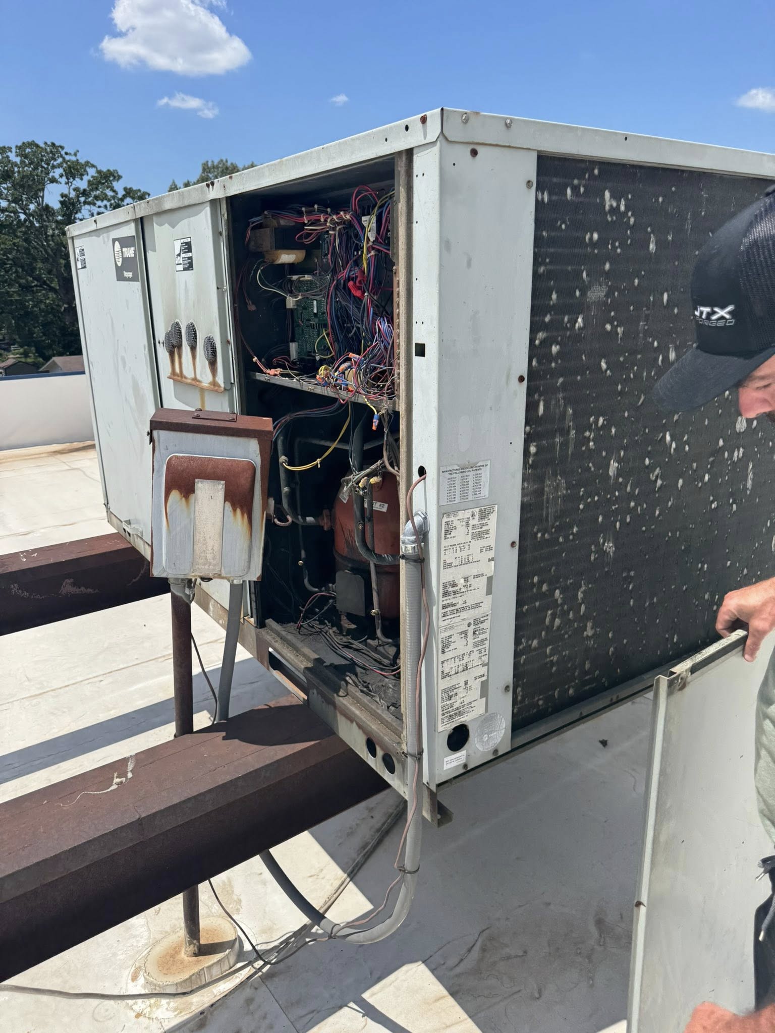 Technician inspecting an open, aging Trane rooftop HVAC unit with exposed wiring, rust, and a dirty condenser coil