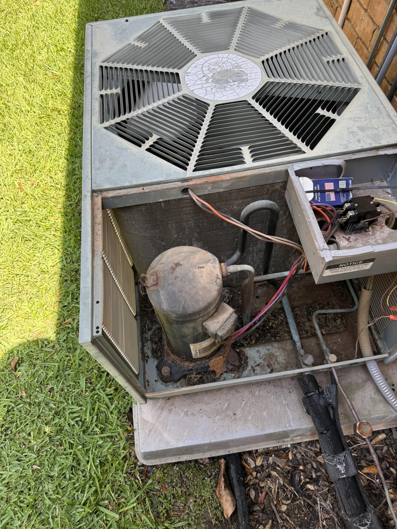 Outdoor AC condenser unit with panel removed, exposing a dirty, corroded compressor and wiring inside