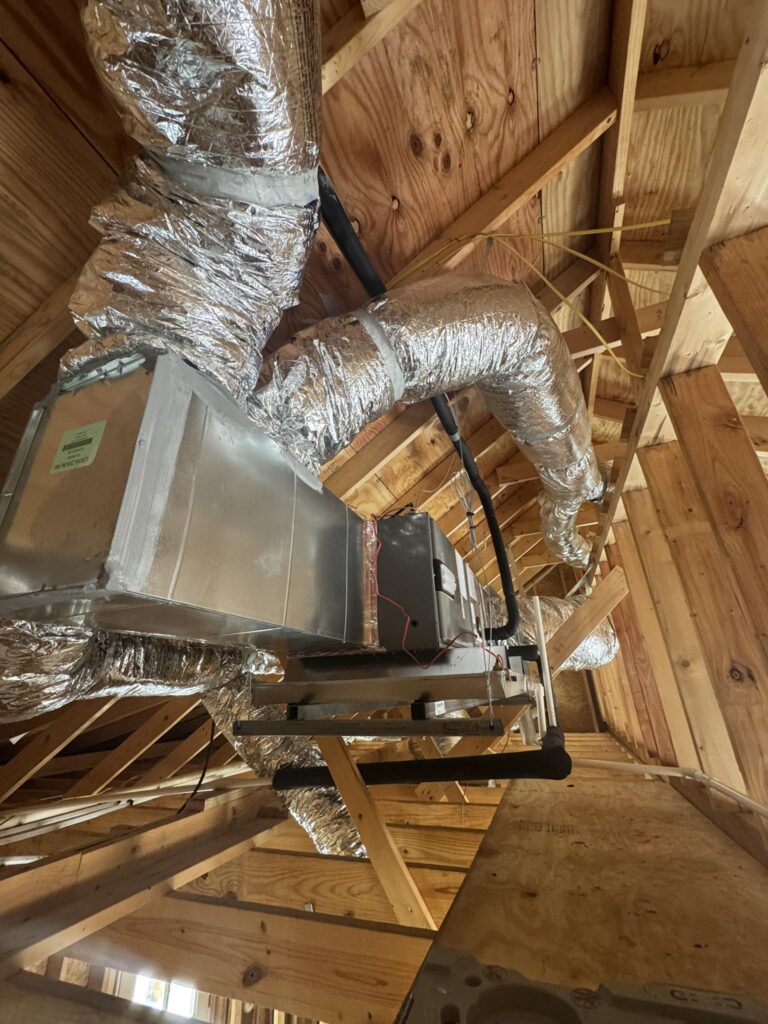 HVAC air handler unit with flexible insulated ductwork installed in a wood-framed attic space during new construction