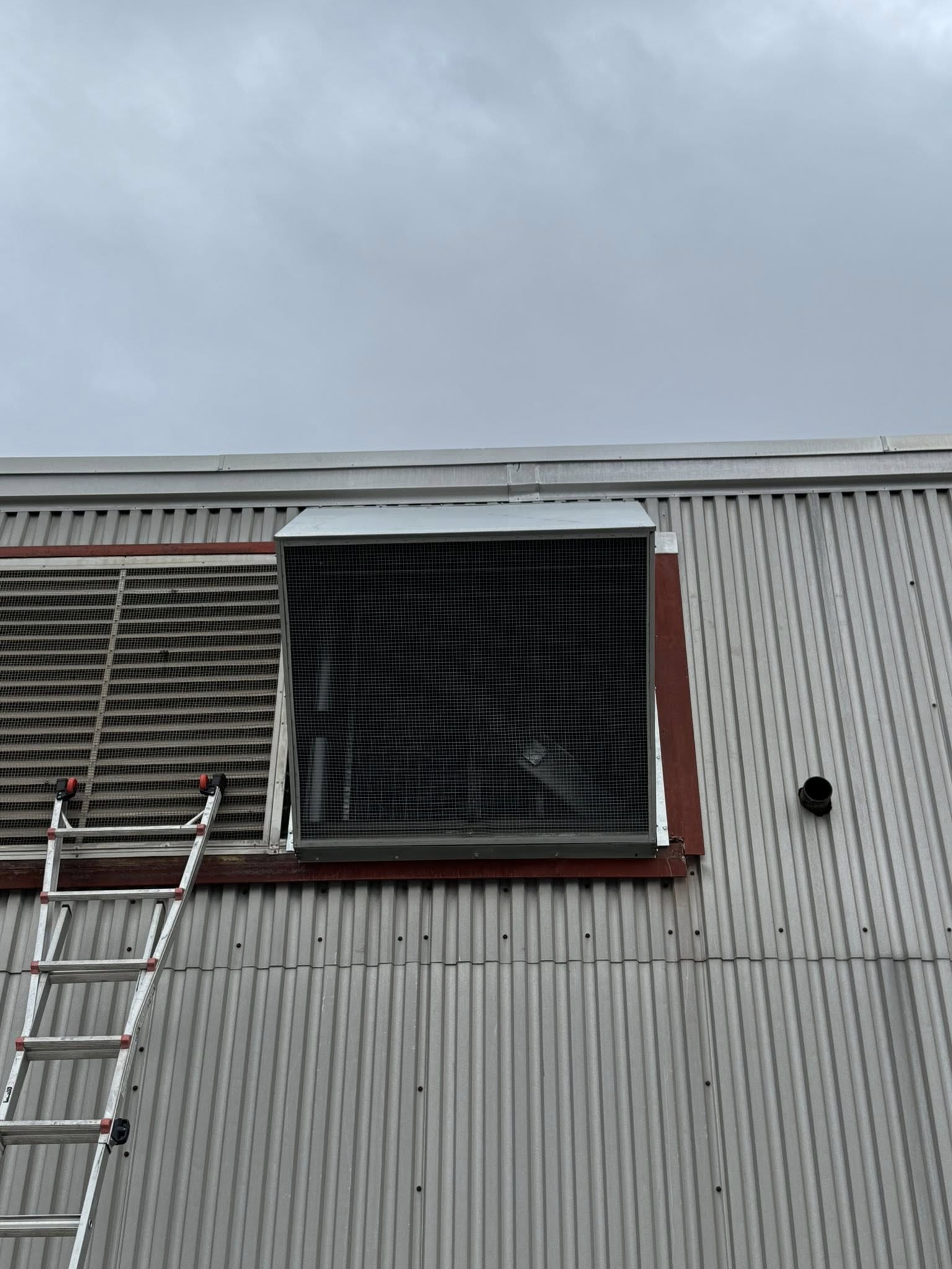 Large industrial ventilation unit mounted on the exterior wall of a metal building, with a ladder leaning against it