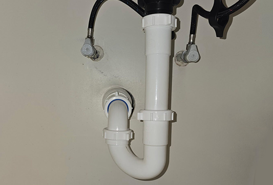 White P-trap drain pipe beneath a sink with braided supply lines connected above